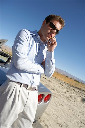 Man using cell phone by sports car at side of desert road Stock Photo - Premium Royalty-Free, Code: 694-03693487