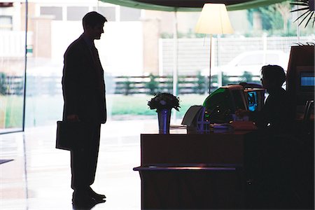 Businessman standing speaking to receptionist, silhouette Stock Photo - Premium Royalty-Free, Code: 695-05764495