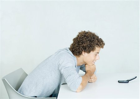 Teenage boy with head down on arms, looking at cell phone Stock Photo - Premium Royalty-Free, Code: 695-05764794