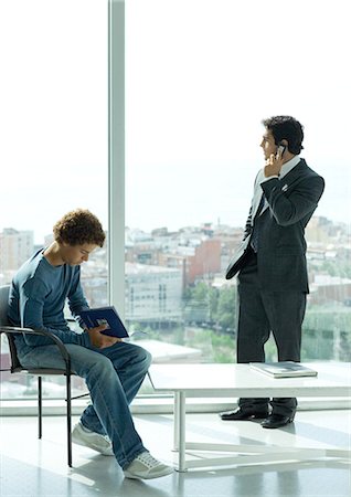 simsearch:6108-05868176,k - Waiting room, casually dressed young man sitting in chair while businessman uses phone by window Foto de stock - Sin royalties Premium, Código: 695-05764837