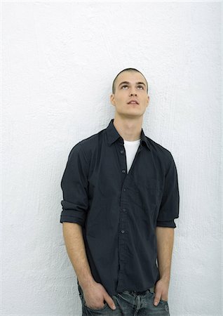 Young man standing looking up, hands in pockets, portrait Stock Photo - Premium Royalty-Free, Code: 695-05765001