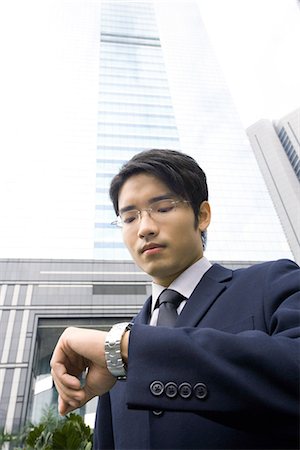 simsearch:695-05770428,k - Businessman standing checking time on wristwatch, skyscraper in background Stock Photo - Premium Royalty-Free, Code: 695-05765036