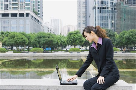 Businesswoman using laptop by water in office park Stock Photo - Premium Royalty-Free, Code: 695-05765051