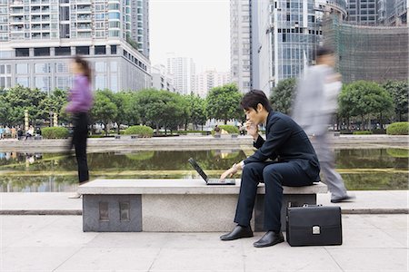 simsearch:695-03378158,k - Businessman using laptop in office park, passers-by blurred in background Fotografie stock - Premium Royalty-Free, Codice: 695-05765061