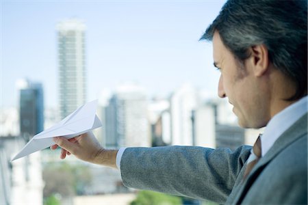 paper airplane - Businessman holding out paper airplane, skyline in background Stock Photo - Premium Royalty-Free, Code: 695-05765189