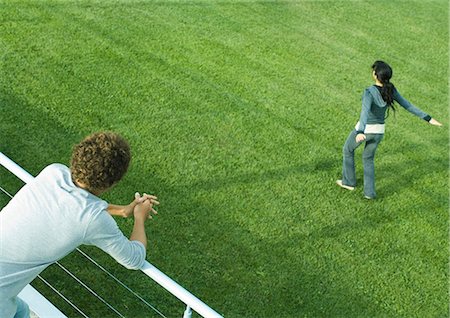 Teenage boy leaning on railing, watching teenage girl spinning on grass Stock Photo - Premium Royalty-Free, Code: 695-05765236