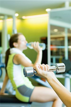 Woman drinking bottle of water, focus on second woman's arm holding dumbbell in foreground Stock Photo - Premium Royalty-Free, Code: 695-05765335