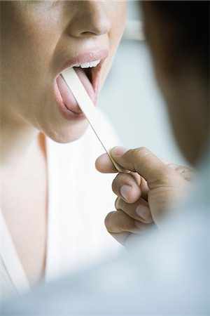 Doctor holding down woman's tongue with tongue depressor Foto de stock - Sin royalties Premium, Código: 695-05765450