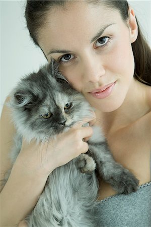 Young woman holding up cat to cheek, smiling at camera Stock Photo - Premium Royalty-Free, Code: 695-05765483