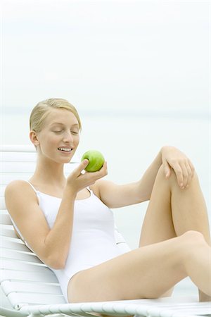 Teenage girl wearing bathing suit, sitting in lounge chair, holding apple Stock Photo - Premium Royalty-Free, Code: 695-05765568