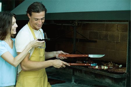 Man tending barbecue, while woman holds up glass of wine for him Foto de stock - Sin royalties Premium, Código: 695-05765604