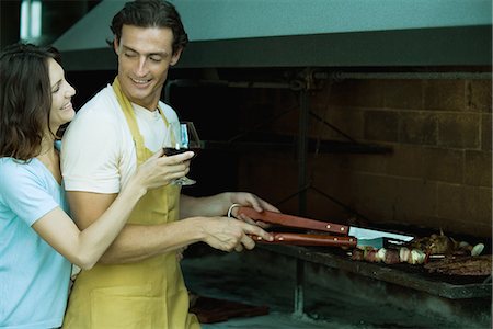 Man tending barbecue, while woman holds up glass of wine for him Stock Photo - Premium Royalty-Free, Code: 695-05765605