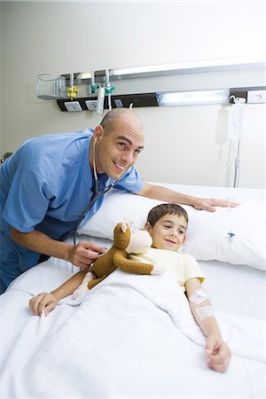 Boy lying in hospital bed, doctor holding stethoscope to stuffed monkey Stock Photo - Premium Royalty-Free, Code: 695-05765977