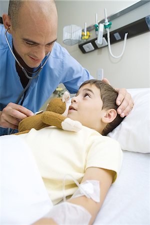 Boy lying in hospital bed, doctor holding stethoscope to stuffed monkey Stock Photo - Premium Royalty-Free, Code: 695-05765978