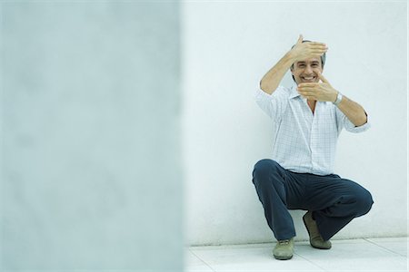 finger frame - Mature man crouching, framing face with hands, smiling Stock Photo - Premium Royalty-Free, Code: 695-05766264