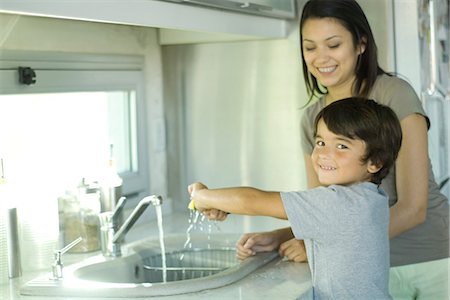 Boy helping mother wash dishes, looking over shoulder at camera Stock Photo - Premium Royalty-Free, Code: 695-05766379