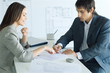 signing contract on computer - Female real estate agent pointing to document, man signing, blueprints in foreground and background Stock Photo - Premium Royalty-Free, Code: 695-05766422