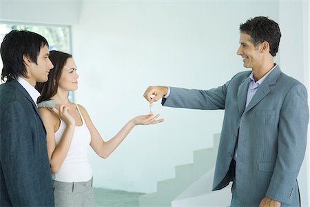 female real estate agent - Real estate agent holding out keys to young couple, standing in bare home interior Foto de stock - Sin royalties Premium, Código: 695-05766446