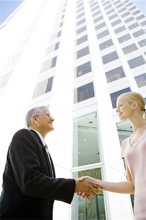 Mature businessman shaking young businesswoman's hand in front of building, low angle view Stock Photo - Premium Royalty-Free, Code: 695-05766528