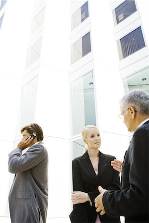 simsearch:695-05776257,k - Two business associates standing, discussing, man using cell phone in background Stock Photo - Premium Royalty-Free, Code: 695-05766529