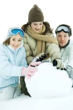 simsearch:696-03401767,k - Three young friends crouching in snow, making large snowball together, two smiling at camera Stock Photo - Premium Royalty-Free, Code: 695-05766586