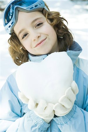 Girl holding heart made of snow, smiling at camera, portrait Stock Photo - Premium Royalty-Free, Code: 695-05766603
