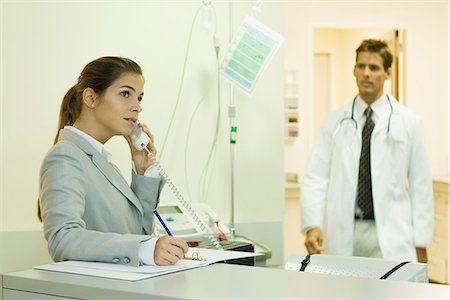 Woman using phone in doctor's office, doctor approaching in background Stock Photo - Premium Royalty-Free, Code: 695-05766635