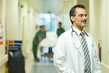 simsearch:400-07334526,k - Male doctor looking away, smiling, hospital corridor in background Stock Photo - Premium Royalty-Free, Code: 695-05766645
