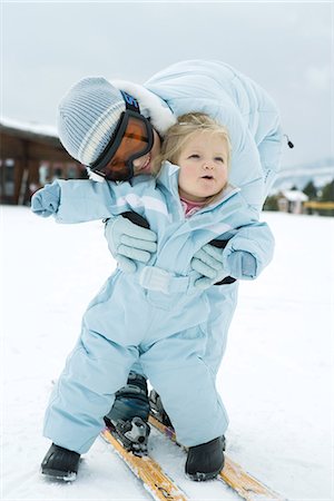 sister hugs baby - Teenage girl bending over, embracing toddler, both dressed in ski-suits Stock Photo - Premium Royalty-Free, Code: 695-05766700