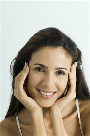 simsearch:695-05766896,k - Woman holding face between hands, smiling at camera, portrait Stock Photo - Premium Royalty-Free, Code: 695-05766911