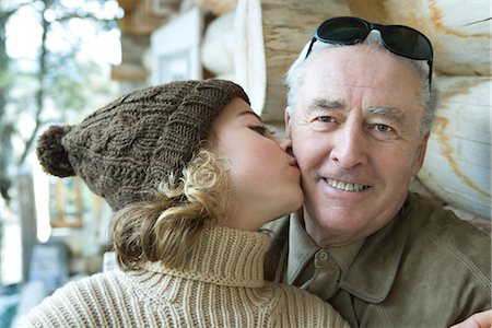 family in log cabin - Senior man smiling at camera, granddaughter kissing him on the cheek, portrait Stock Photo - Premium Royalty-Free, Code: 695-05766988