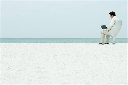 Man using laptop computer at the beach, full length Stock Photo - Premium Royalty-Free, Code: 695-05767039