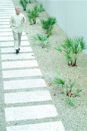 Mature man walking on path, looking at cell phone, full length Stock Photo - Premium Royalty-Free, Code: 695-05767049