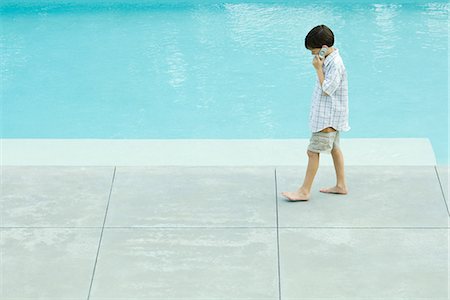 swimming pool phone - Boy walking next to swimming pool, using cell phone, looking down Stock Photo - Premium Royalty-Free, Code: 695-05767080