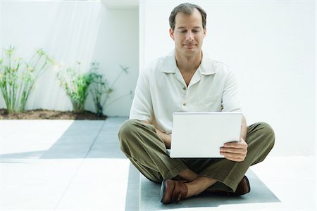 sitting on the ground with a laptop - Man sitting on the ground using laptop computer, smiling, full length Stock Photo - Premium Royalty-Free, Code: 695-05767081