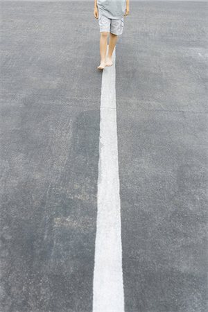 Boy walking along white dividing line, cropped view Stock Photo - Premium Royalty-Free, Code: 695-05767228