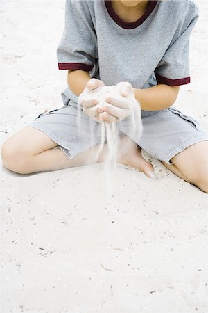 Boy sitting on the ground holding handful of sand, cropped view Stock Photo - Premium Royalty-Free, Code: 695-05767222