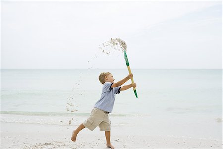 simsearch:695-05767597,k - Young boy at the beach, holding up shovel and throwing sand, side view Fotografie stock - Premium Royalty-Free, Codice: 695-05767243