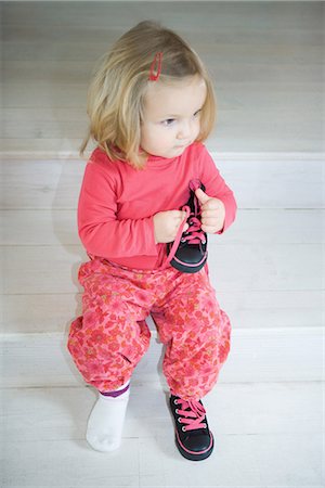 Blonde toddler girl sitting on steps, wearing one shoe, holding other shoe in hand Stock Photo - Premium Royalty-Free, Code: 695-05767366