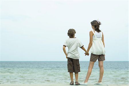 Brother and sister standing at the beach holding hands, looking at view Stock Photo - Premium Royalty-Free, Code: 695-05767421