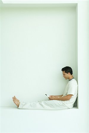 Man sitting on ledge using cell phone, full length, side view Stock Photo - Premium Royalty-Free, Code: 695-05767490