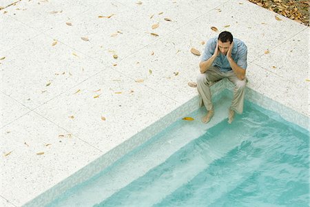 Man sitting with feet in pool, holding head, high angle view Stock Photo - Premium Royalty-Free, Code: 695-05767528