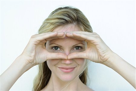 finger frame - Woman looking through finger frame at camera, smiling Stock Photo - Premium Royalty-Free, Code: 695-05767566