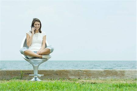 simsearch:695-05768222,k - Teenage girl sitting in chair by the sea, using cell phone, smiling at camera Foto de stock - Sin royalties Premium, Código: 695-05767581