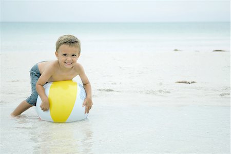 Little boy lying on top of beach ball at the beach, smiling at camera Stock Photo - Premium Royalty-Free, Code: 695-05767590