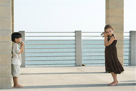 Two young friends playing with tin can phone together, sea in background Foto de stock - Royalty Free Premium, Número: 695-05767600