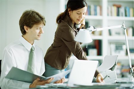 Male and female colleagues at desk, man looking at laptop computer, woman using phone Stock Photo - Premium Royalty-Free, Code: 695-05767648