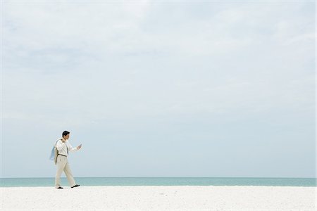 Homme d'affaires marchant sur la plage vide, regardant de téléphone cellulaire Photographie de stock - Premium Libres de Droits, Code: 695-05767668