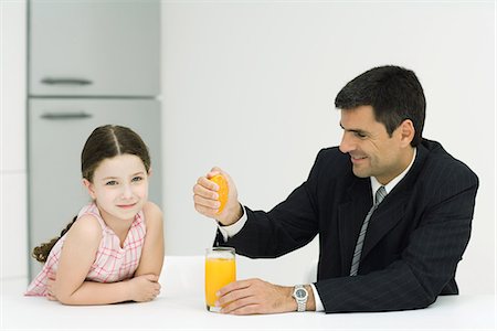 squeezing (make juice) - Father and daughter sitting together at table, man squeezing orange juice into glass, girl smiling at camera Stock Photo - Premium Royalty-Free, Code: 695-05767764