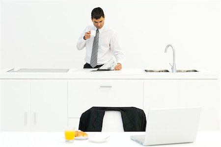 Businessman standing in kitchen, reading newspaper and drinking coffee, breakfast on table in foreground Foto de stock - Sin royalties Premium, Código: 695-05767766